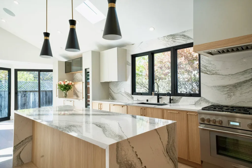Contemporary kitchen with DOCA cabinetry and Cambria quartz countertops, featuring a striking waterfall island, black pendant lighting, and natural wood accents