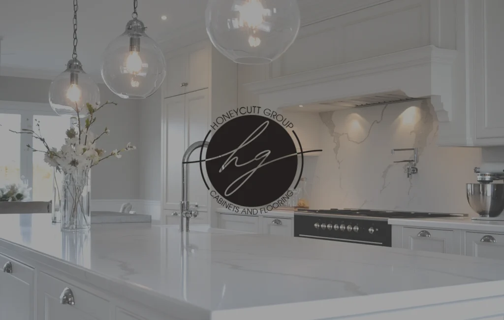 Bright and modern kitchen with white marble countertops, pendant lights, and Honeycutt Group logo overlay in the center