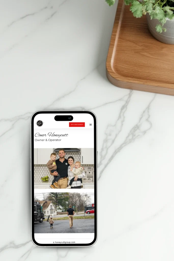 Smartphone resting on a marble countertop, displaying Honeycutt Group's website with a profile of Conor Honeycutt, the owner and operator